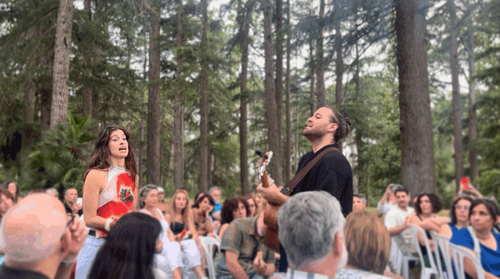 Barcelona-based duo Eva Sola performing live at the opening of El Jardí Sonor in Parc Samà, Cambrils. Eva Menéndez sings with passion while Albert Solà plays the guitar, surrounded by an attentive outdoor audience among the trees.