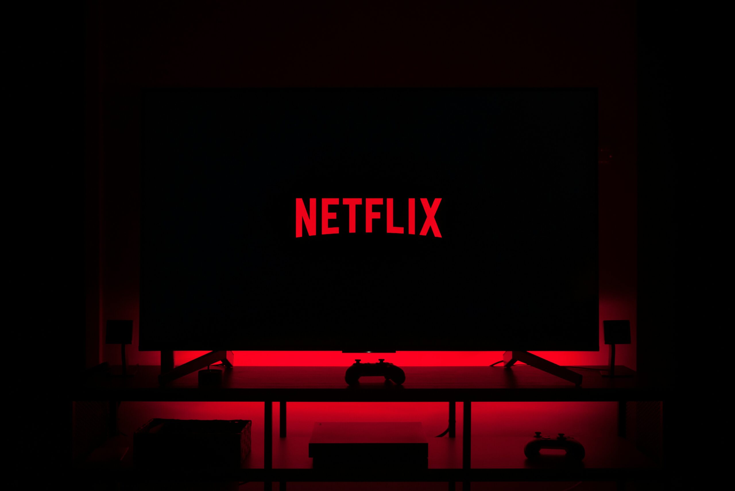 Television screen displaying Netflix logo in a dark room with red ambient lighting.